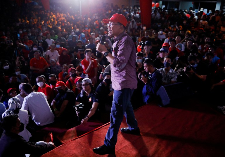 Anwar Ibrahim in a red baseball cap, checked shirt and blue trousers speaks to thousands of supporters at a rally in Kuala Lumpur