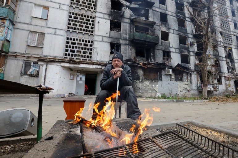 A local resident sits by the fire outside an apartment building heavily damaged in the course of Russia-Ukraine conflict, in Mariupol, Russian-controlled Ukraine, November 16, 2022. REUTERS/Alexander Ermochenko