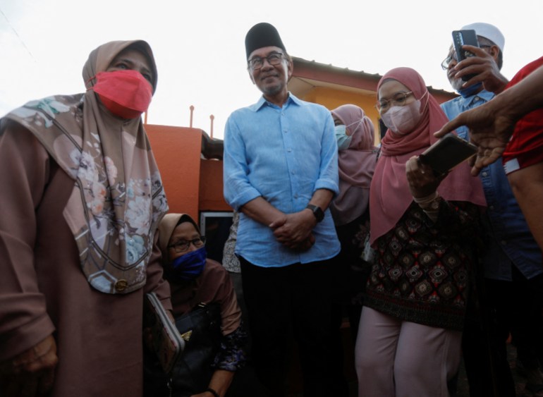 Anwar en chemise bleue et songkok, debout parmi un groupe d'hommes et de femmes après avoir voté.  Il a l'air détendu