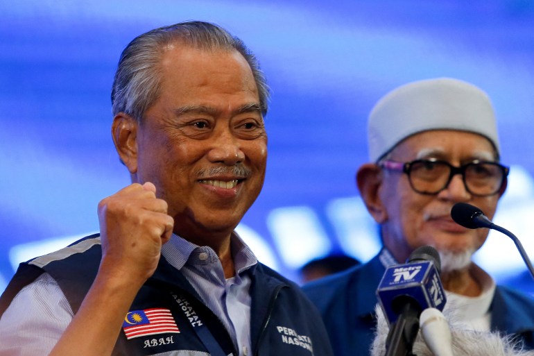 Close-up of Muhyiddin clenching his fist and grinning with PAS leader Hadi Abdul Awang standing next to him.  He looks satisfied