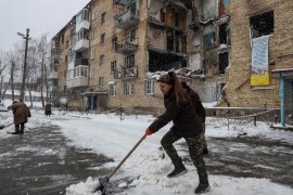 A local resident shovels snow near her destroyed building in the Ukrainian village of Horenka, which was heavily damaged by fighting in the early days of the Russian invasion [Gleb Garanich/Reuters]