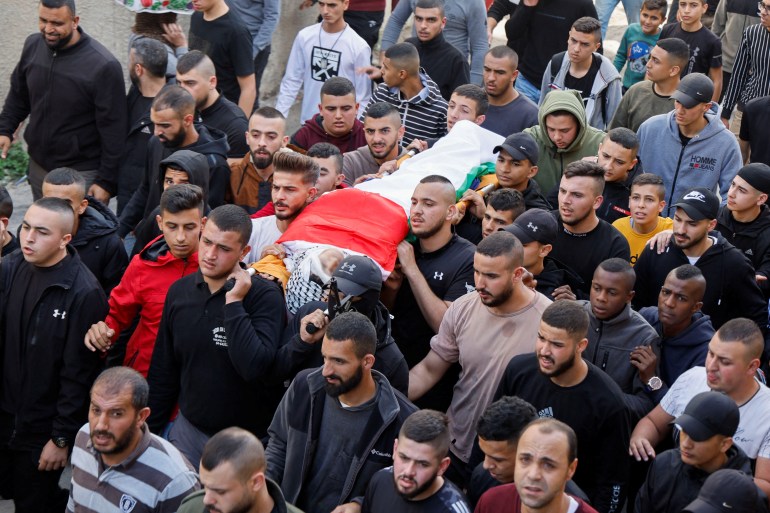 Crowd marches carrying a dead body wrapped in a palestinian flag
