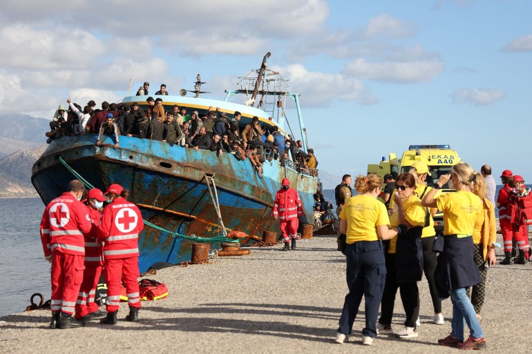 Red Cross volunteers and rescue crews stand next to a fishing boat carrying migrants at the port of Paleochora