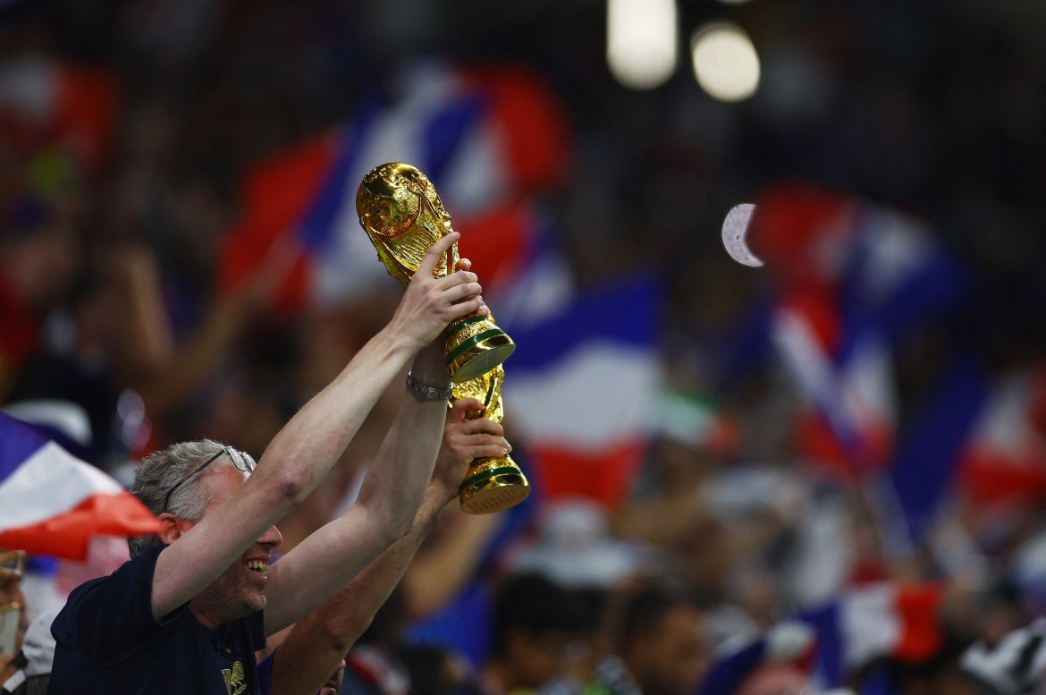 Fans hold World Cup replica against a blurred background of French flags in the stadium