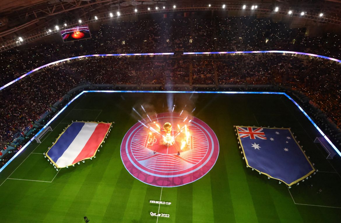 Bird's eye view of the pitch, where many people hold up a flag of Australia and France on each side of a big glowing trophy