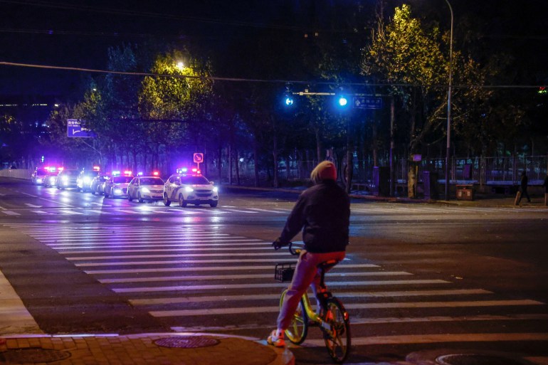 Carros de polícia com luzes piscando se alinham ao longo de uma rua de Pequim, onde havia rumores de que um protesto ocorreria.