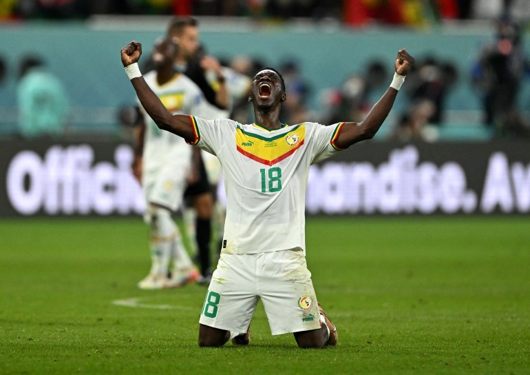 Senegal's Ismaila Sarr celebrates qualifying for the knockout stages by crying on her knees as she raises her arms in victory.