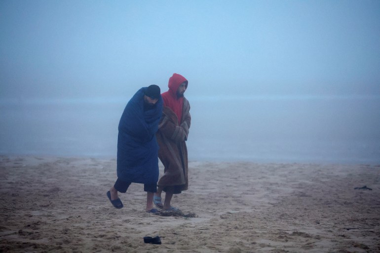 Two migrants from Syria, wearing sandals and using sleeping bags to keep themselves warm, walk on the beach in Bleriot-Plage, one of the beaches used by migrants to leave by small dinghies the coast of northern France to cross the English Channel in an attempt to reach Britain