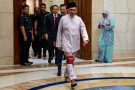 Anwar Ibrahim striding into the Prime Minister's office on his first day on the job. He is wearing a traditional outfit and looks purposeful