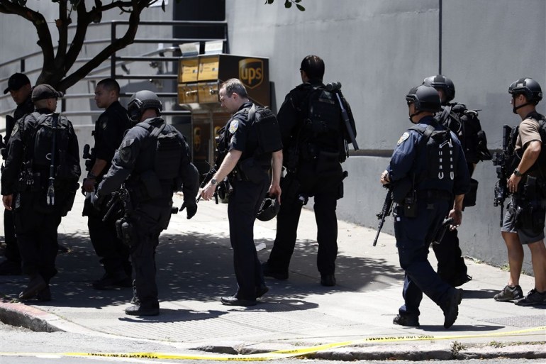Oficiais da SWAT de San Francisco em frente a um prédio onde ocorreu um tiroteio.  Eles estão em uniformes militares pretos e carregando armas