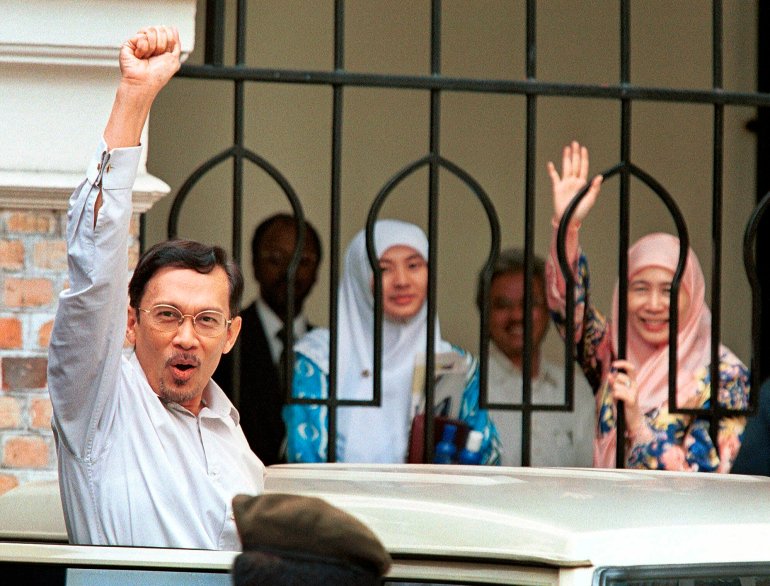 Anwar punching the air as he arrives at court in 1998. He looks defiant. His wife and eldest daughter are also watching and waving to supporters