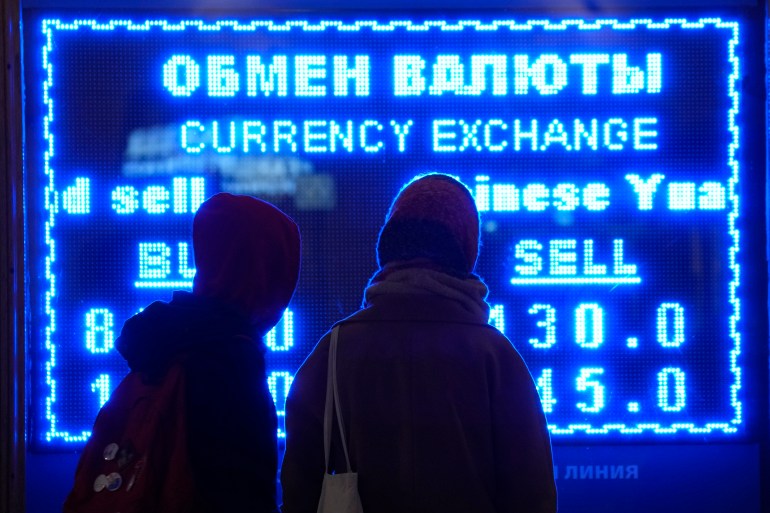 Women look at a screen displaying exchange rate at a currency exchange office in St. Petersburg