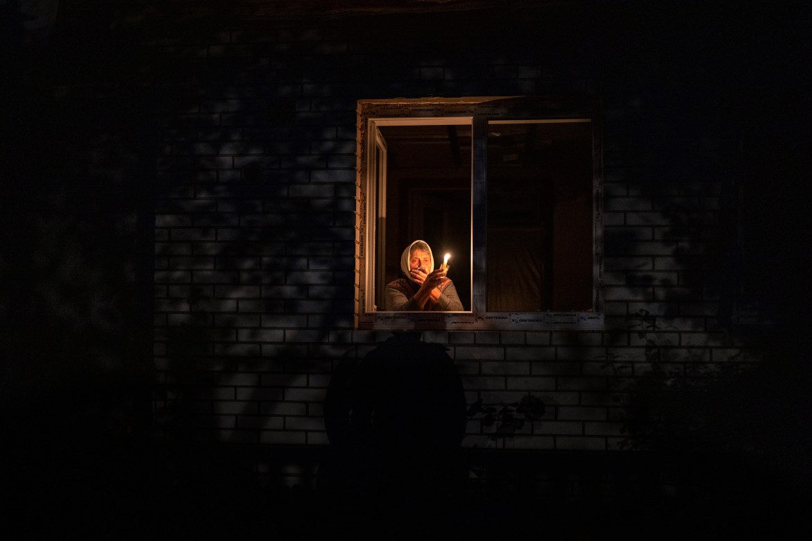 Catherine, 70, looks out the window while holding a candle for light inside her house during a power outage.