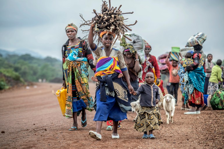 Women wearing colourful clothes, one carrying a yellow petrol canister and others bags of food on their head, flee fighting between M23 rebels and Congolese forces . There are also goats and children in the line of people.