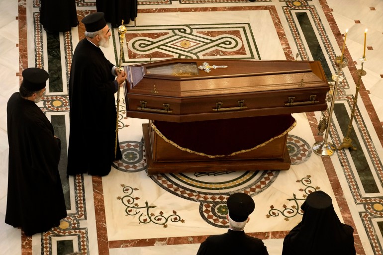 A Christian Orthodox priest stands in front of the coffin 