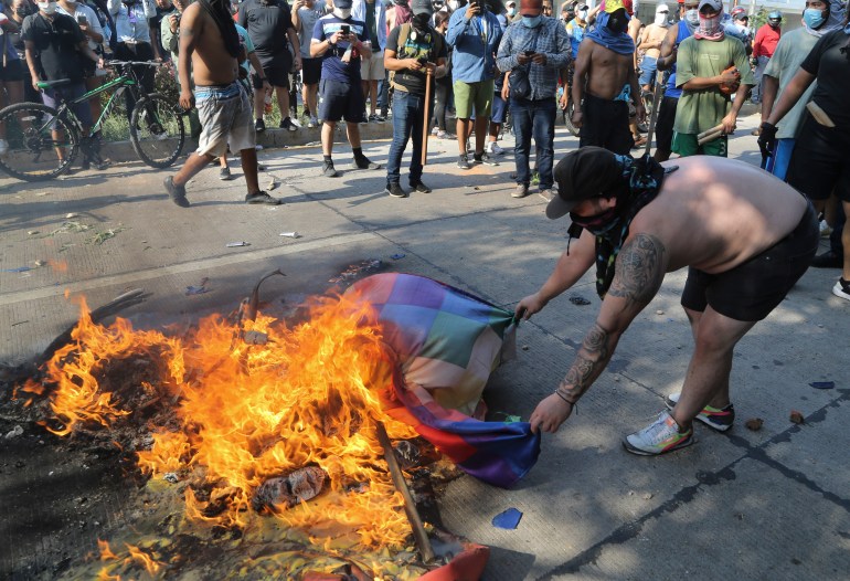 Een demonstrant houdt de randen van een veelkleurige vlag vast terwijl deze in een straat in Santa Cruz brandt