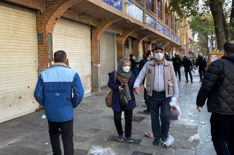 People walk in front of closed shops of Tehran's Grand Bazaar as anti-riot police controls the protest scene, Iran