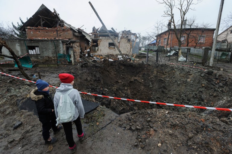 Two children look at the crater, cordoned off by police tape, with houses behind the crater damaged by the blast
