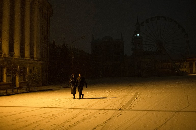 Karla kaplı bir Kiev caddesinde elektrik kesintileri nedeniyle karanlıkta iki kişi yürüyor