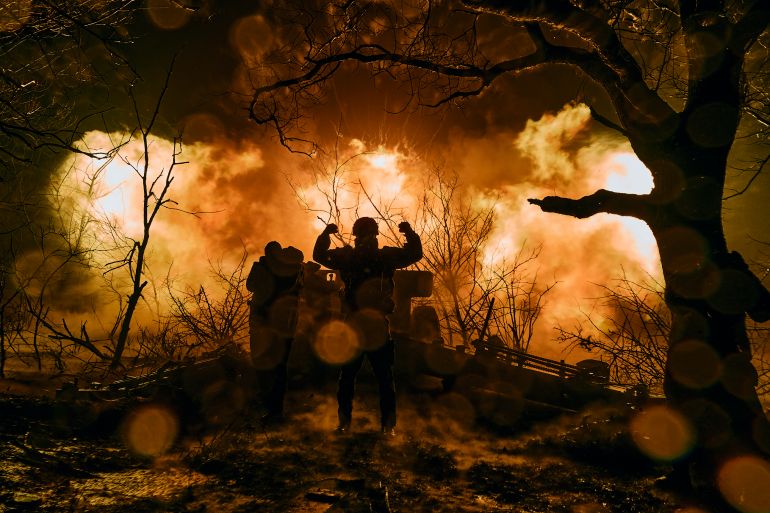 A Ukrainian soldier with his arms up in the air silhouetted against the flames of an explosion after firing artillery shells near Bakhmut, Ukraine.