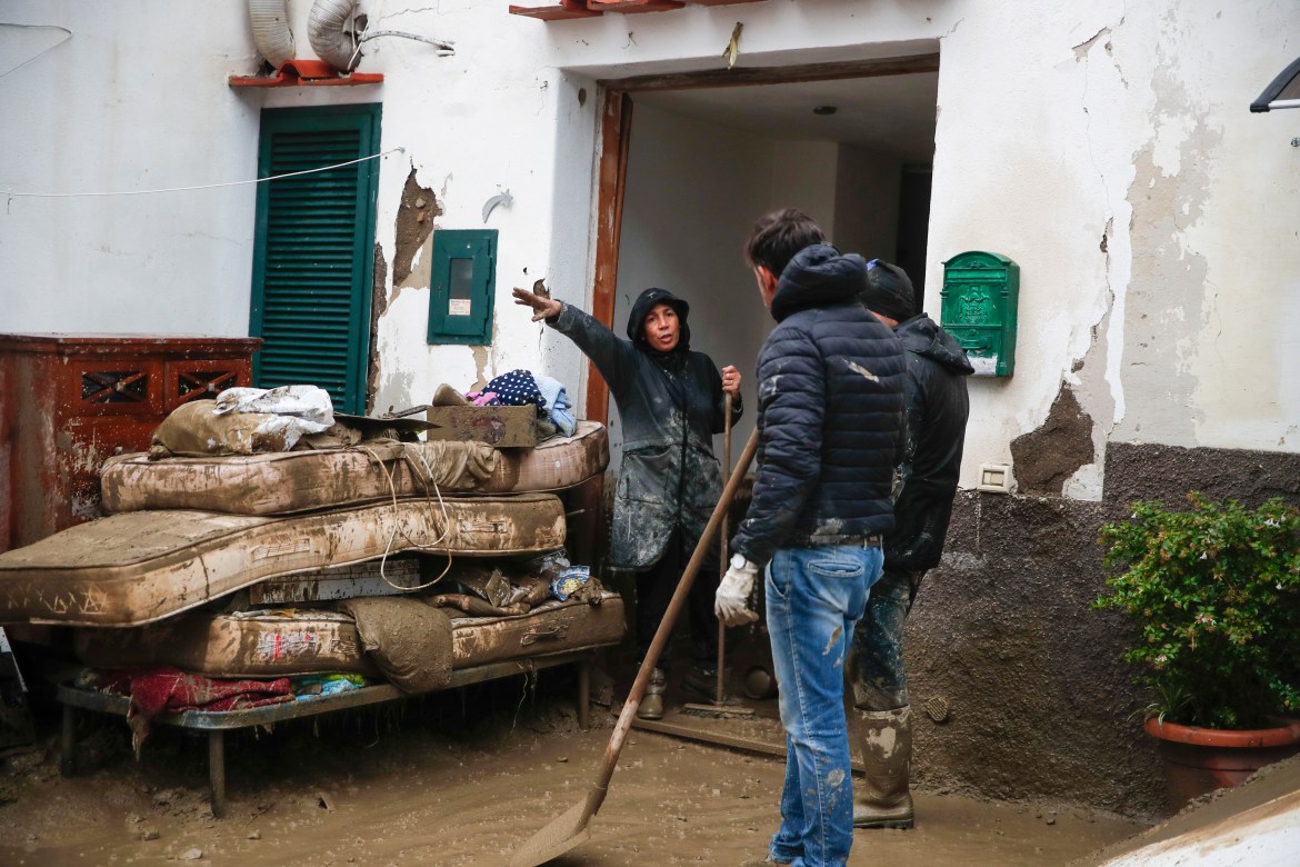 People remove mud from a house after heavy rainfall triggered landslides