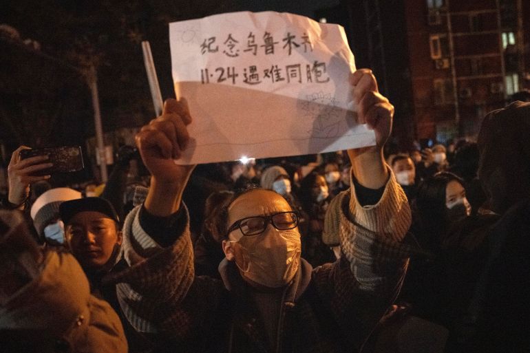 A masked protester holds up a sign which reads "Commemorate Urumqi Nov 24 compatriots who died" in Beijing