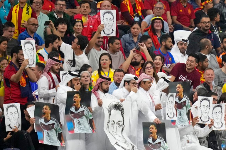 Spectators hold photos of former German international player Mesut Ozil on the stands and cover their mouths during the World Cup group E football match between Spain and Germany at the Al Bayt Stadium in Al Khor , Qatar.