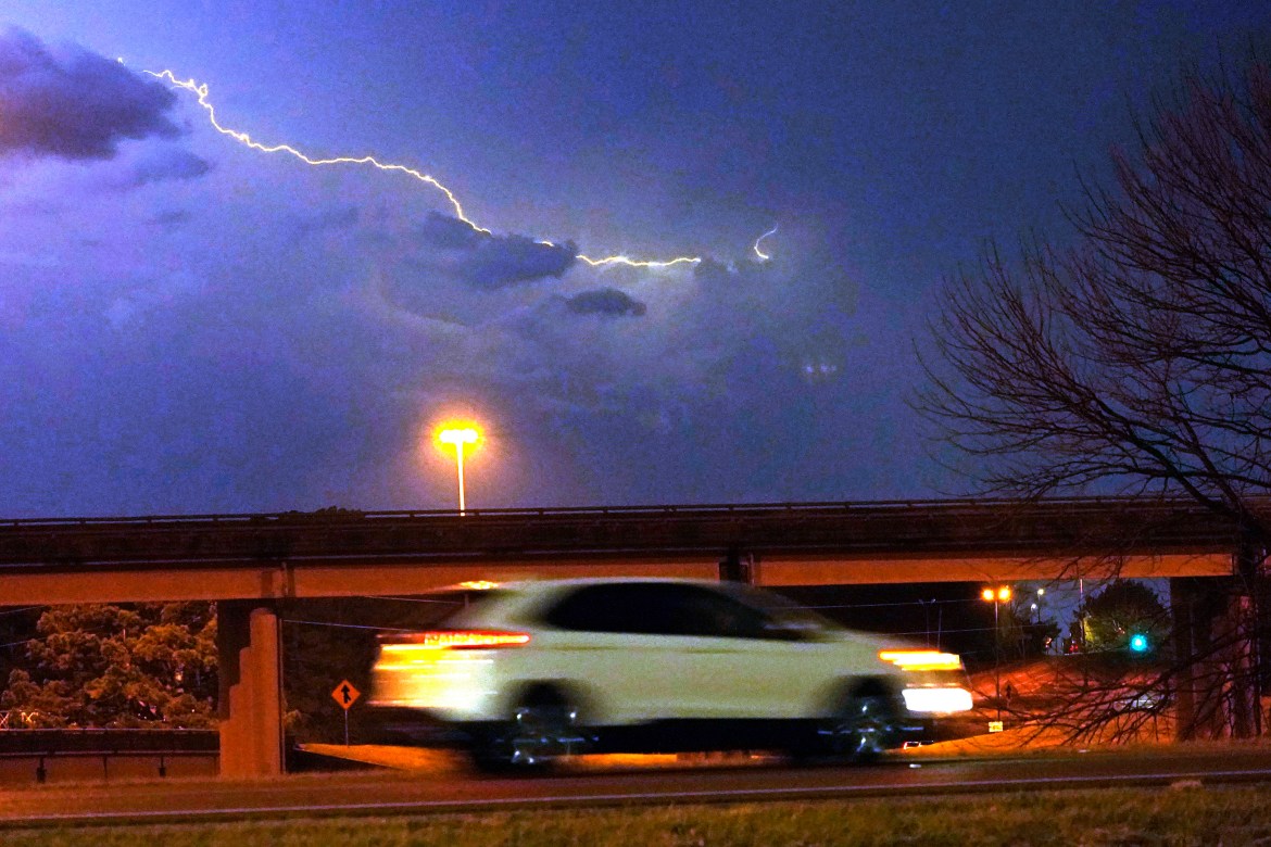 A vehicle races along a Jackson, Miss., street as lightning streaks across the sky