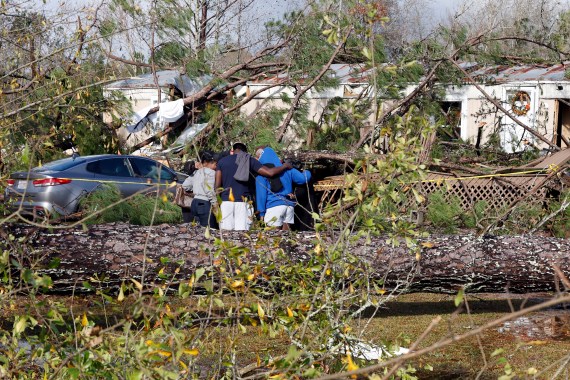 Friends and family pray outside a damaged mobile home,