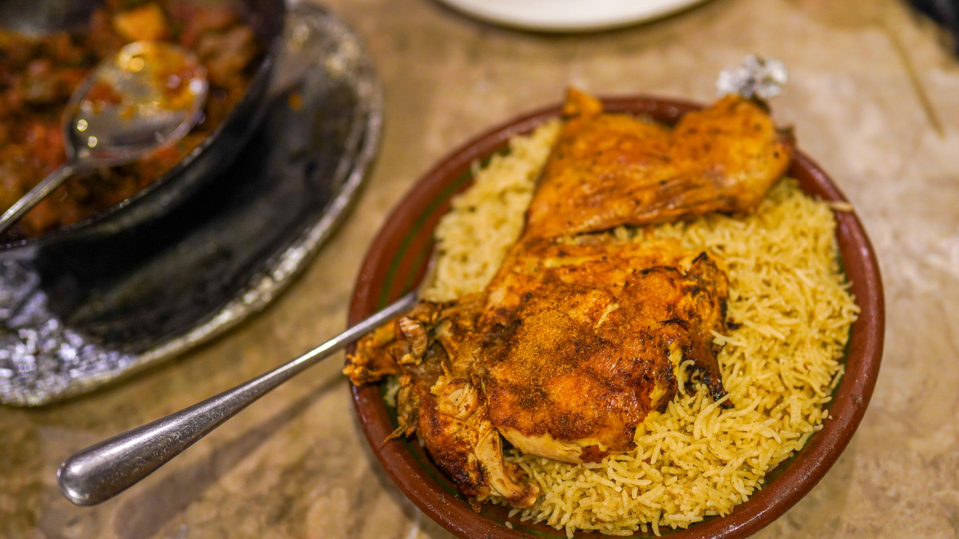 A clay bowl of spiced rice with half a grilled chicken sajji on top