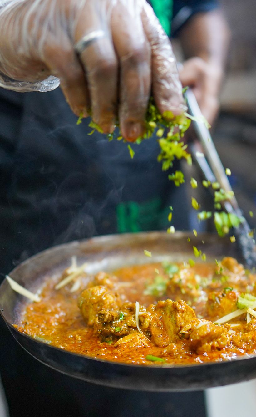 chef's hands sprinkling parsley on a pan of chicken karahi