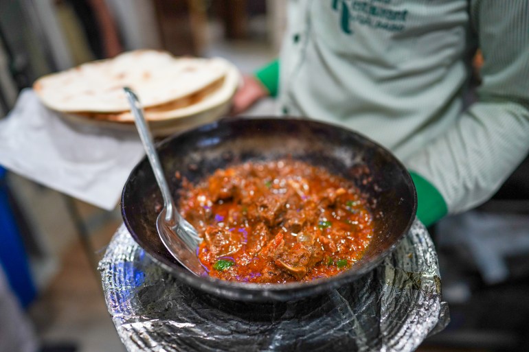 A waiter taking a pan of mutton karahi out in one hand and a plate of naan in the other