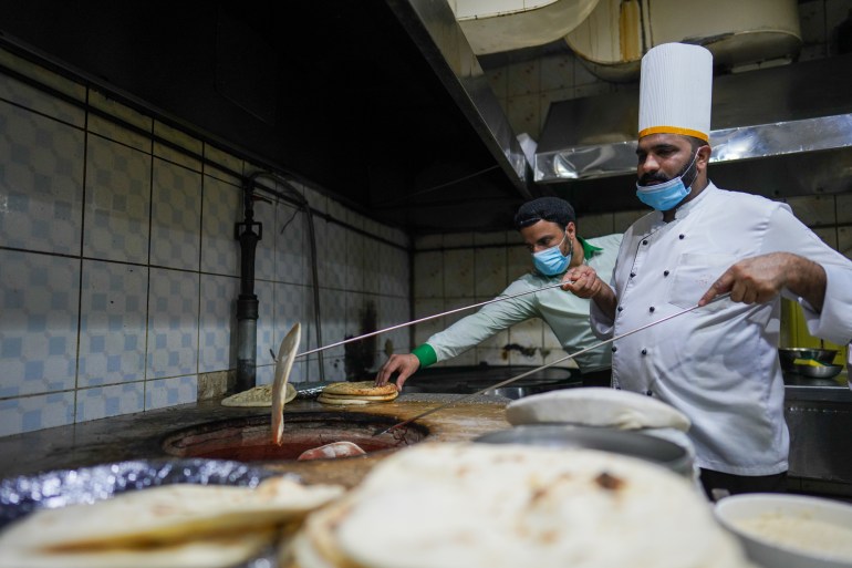 Chef Hussein pulls bread out of the tandoor as a waiter reaches for a pile of cooked naan on the side