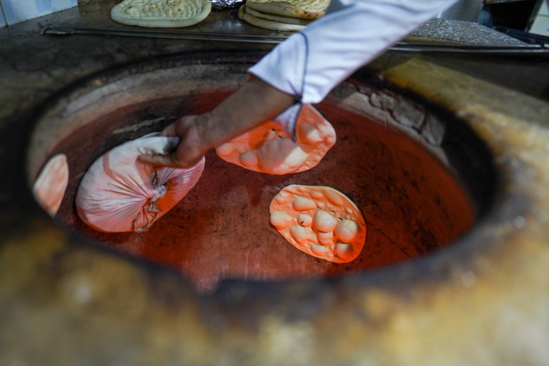 A view of the tandoor as a cook uses a round pillow-like pad to put rounds of dough on the blazing hot walls