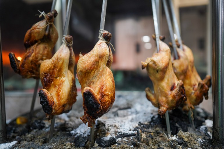 Skewered chickens hanging upside down around a coal fire where they've been cooking for hours. Their skin is well-crisped