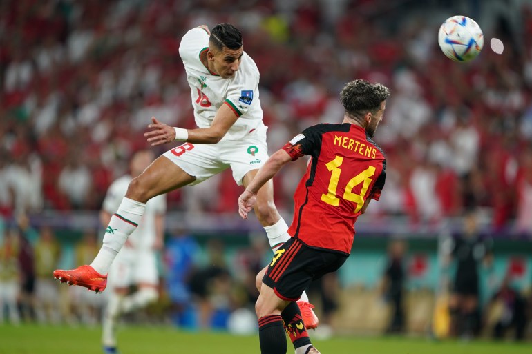 A Moroccan player in midair as a Belgian player next to him looks back in the Group F, FIFA World Cup 2022 game between Morocco and Belgium.