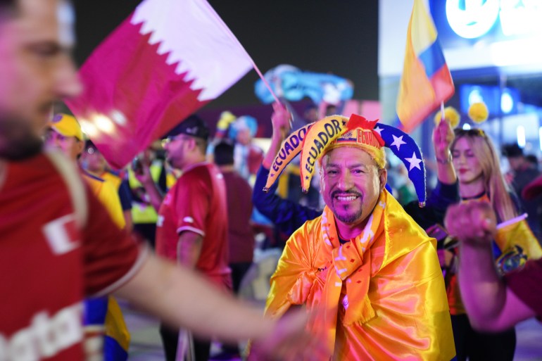 Ecuadoriaanse fans vieren feest buiten het Al Bayt-stadion.  Een van hen, met een narrenhoed in de kleuren van Ecuador, glimlacht naar de camera 