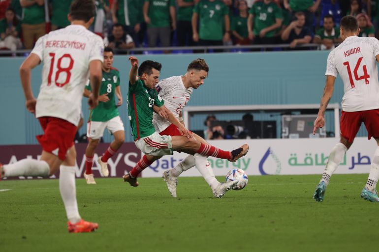 Mexican and Polish players tackle for the ball during their match at Stadium 974 in Ras Abu Aboud, Qatar.