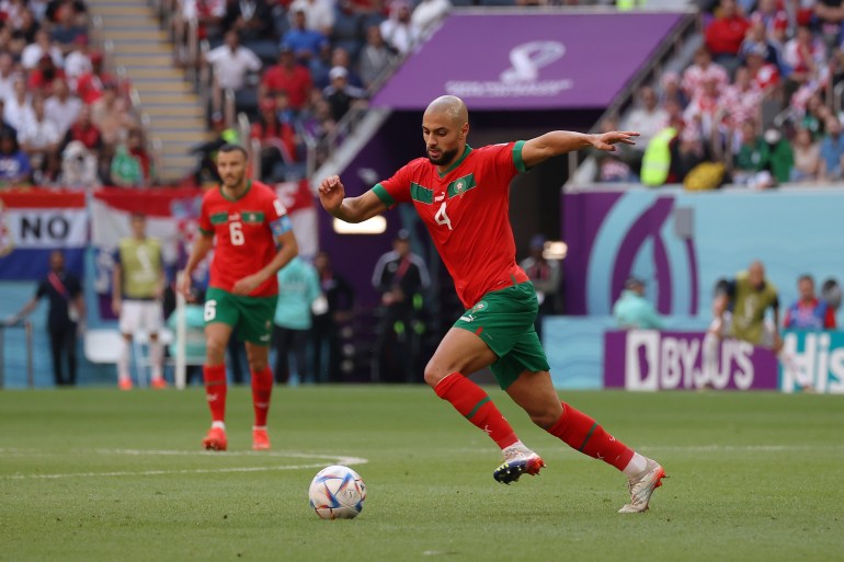 Moroccan player with arms outstretched, in motion, to kick the ball