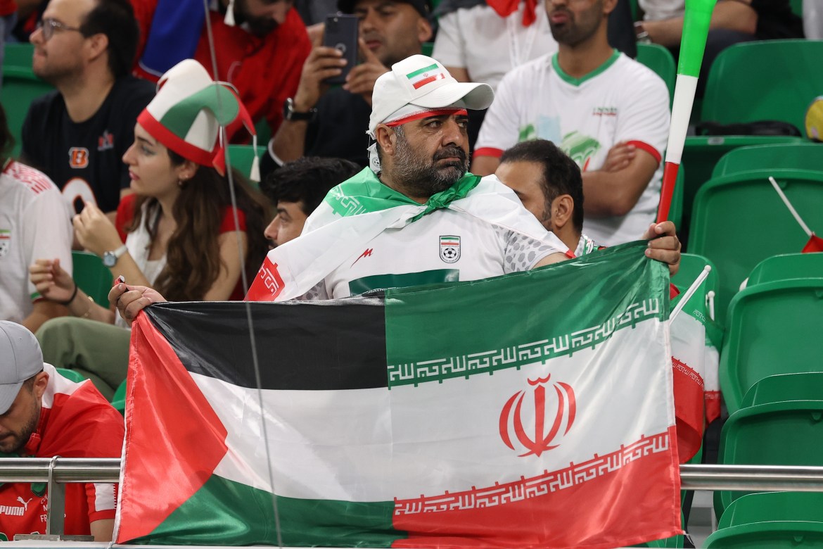 Iranian fan holdds Palestinian and Iranian flags as fans celebrating in the stands before the match