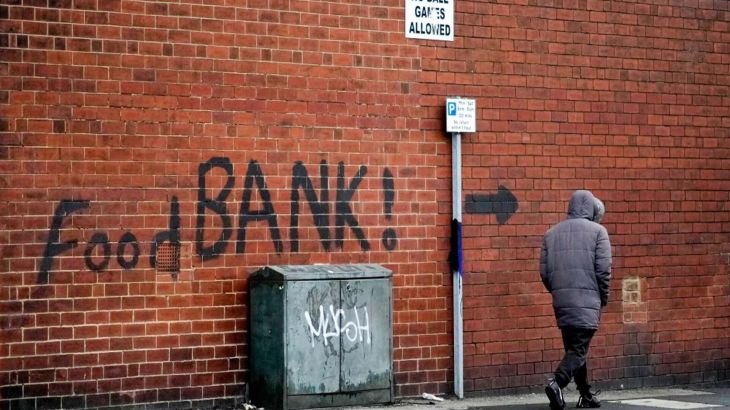 A man walks past the words 'Food Bank' on a wall in the UK
