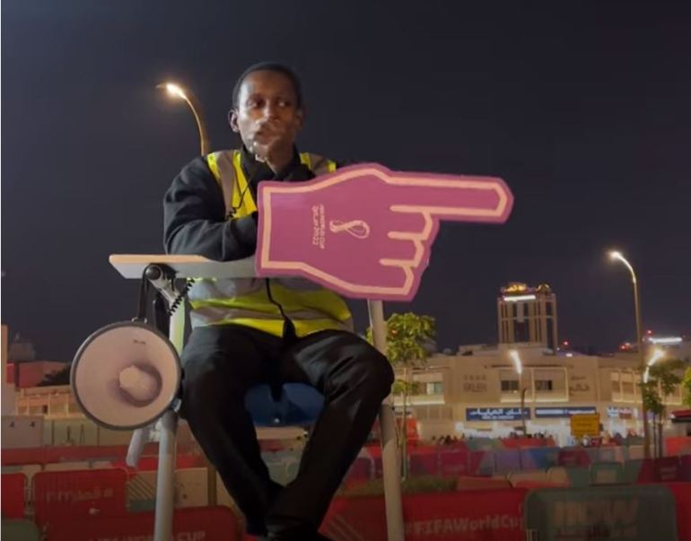 Abubakr Abbass op een scheidsrechtersstoel, wijzend naar een gigantische kartonnen hand