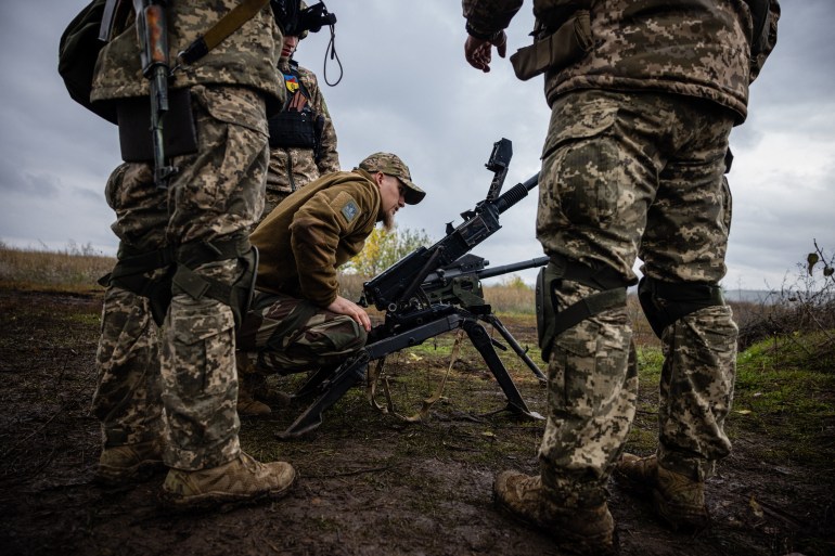 Soldados ucranianos verificam suas armas na linha de frente em Donetsk.  Há três homens e um está verificando a arma enquanto os outros dois estão de costas para a câmera