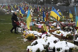 A woman visits snow-covered graves of Ukrainian soldiers killed since the Russian invasion. Ukrainian flags are flying around the graves where people have left flowers