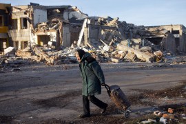 An elderly woman pulls a bag past a destroyed building in Bakhmut, Donetsk region [Yevhen Titov/AFP]