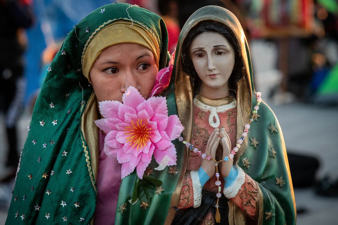 A pilgrim stands next to an image of the Virgin of Guadalupe