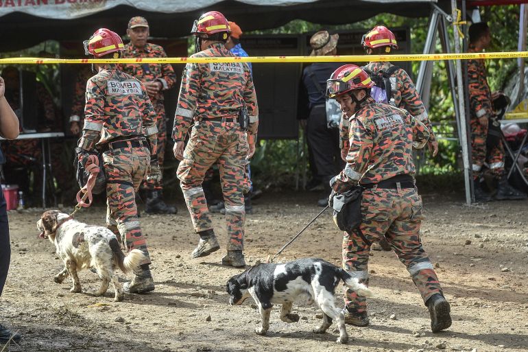 Rescue workers walk with sniffer dogs at the site of a deadly landslide as they search for survivors in Batang Kali, Selangor on December 17, 2022. - Rescue workers scoured muddy terrain for survivors and bodies on December 17 as the death toll from a landslide at a Malaysian campsite rose to 21, including five children, authorities said. (Photo by Arif Kartono / AFP)