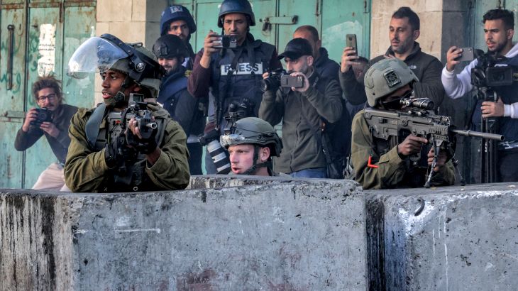 Israeli soldiers, flanked by journalists, take cover behind concrete barriers amidst clashes