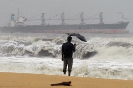 A man holding an umbrella watches large waves on Chennai&#39;s Marina beach in Tamil Nadu state [File: Babu/Reuters]