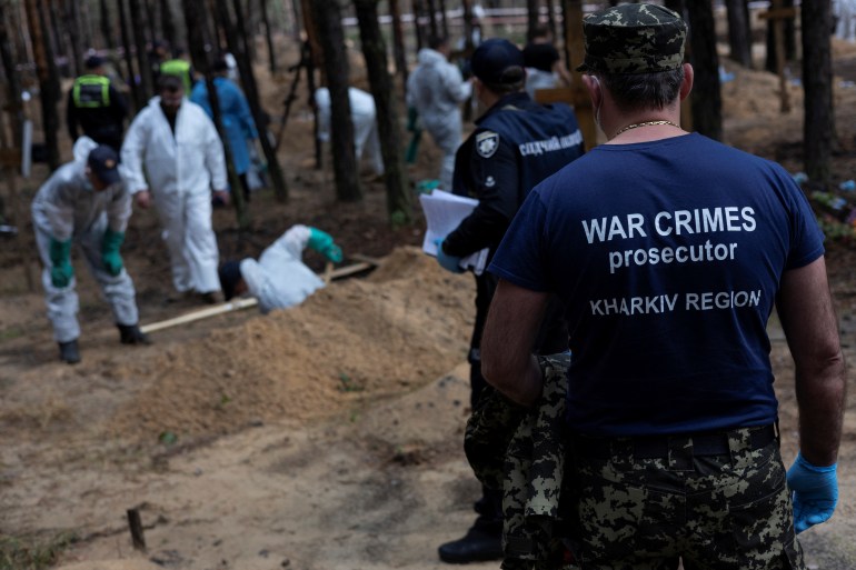 A war crimes prosecutor stands as experts work at a forest grave site during an exhumation, as Russia's attack on Ukraine continues, in the town of Izium, recently liberated by Ukrainian Armed Forces, in Kharkiv region, Ukraine September 18, 2022. REUTERS/Umit Bektas